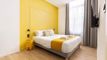 Quarto de hotel moderno com cama, mesa de cabeceira, televisão na parede e janela com cortinas.