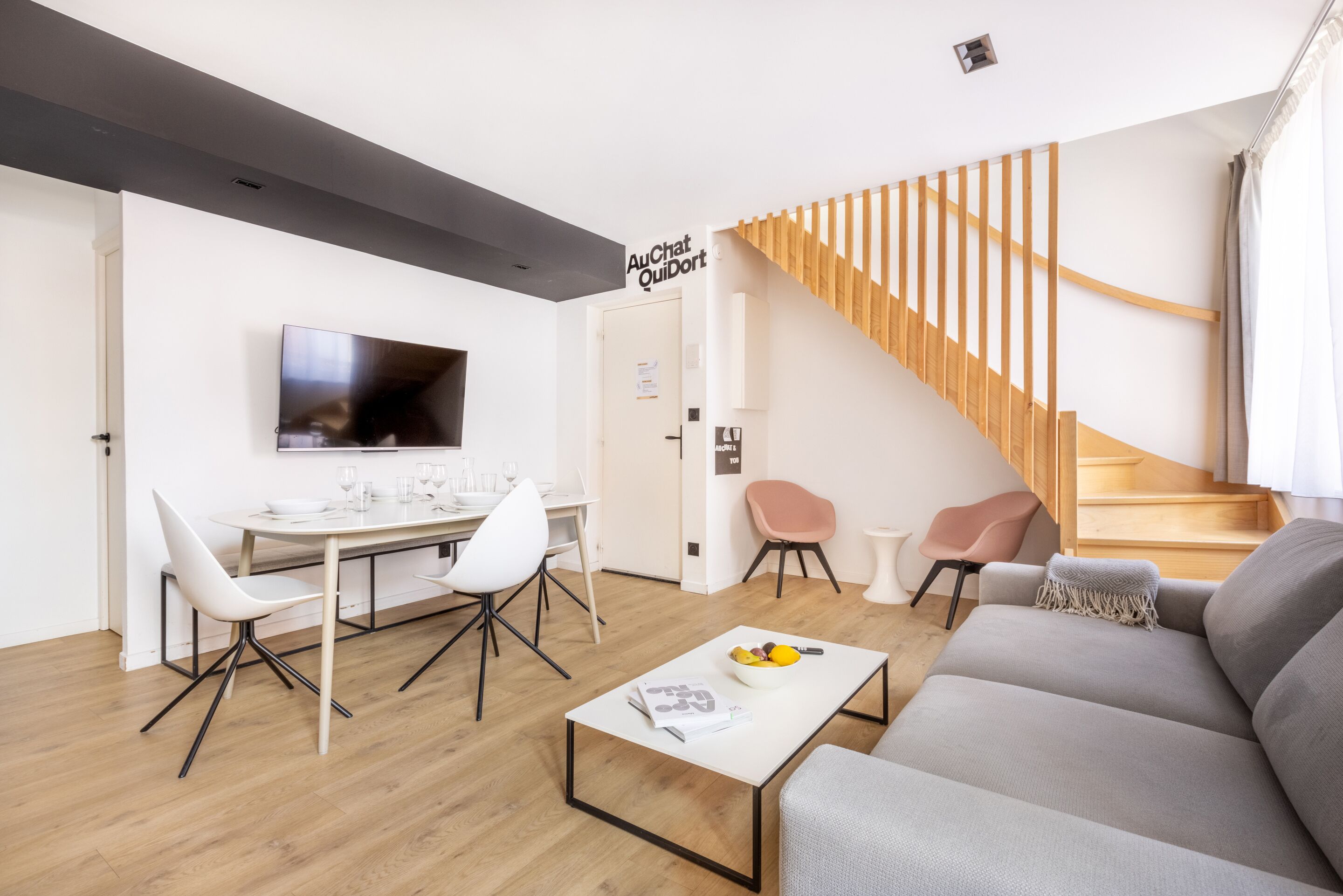 Uma sala de estar moderna com área de jantar, escada e TV de tela plana na parede.