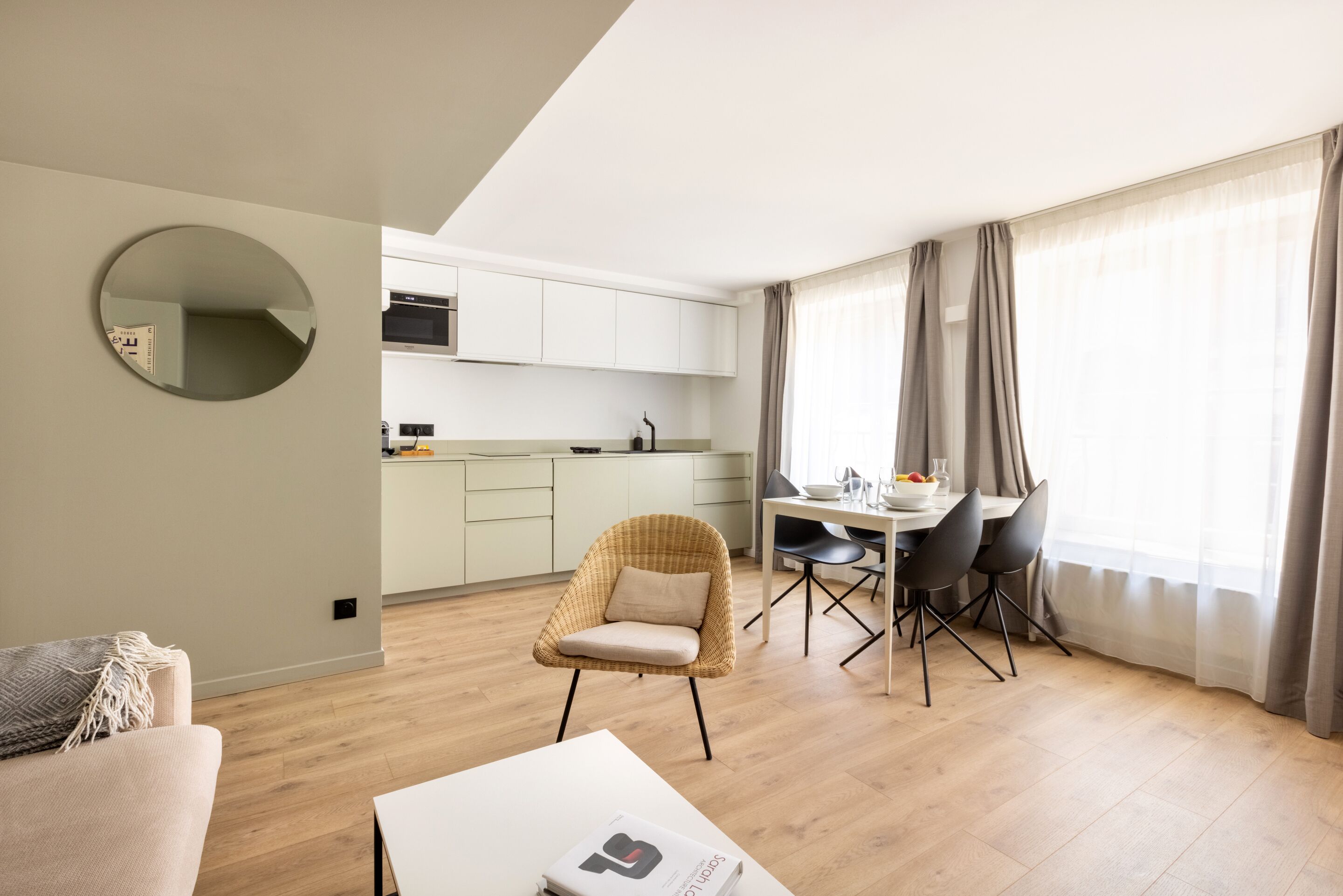 Un salon moderne avec un grand miroir rond, un canapé, une table à manger avec des chaises et un coin cuisine équipé de placards et d’un four à micro-ondes.