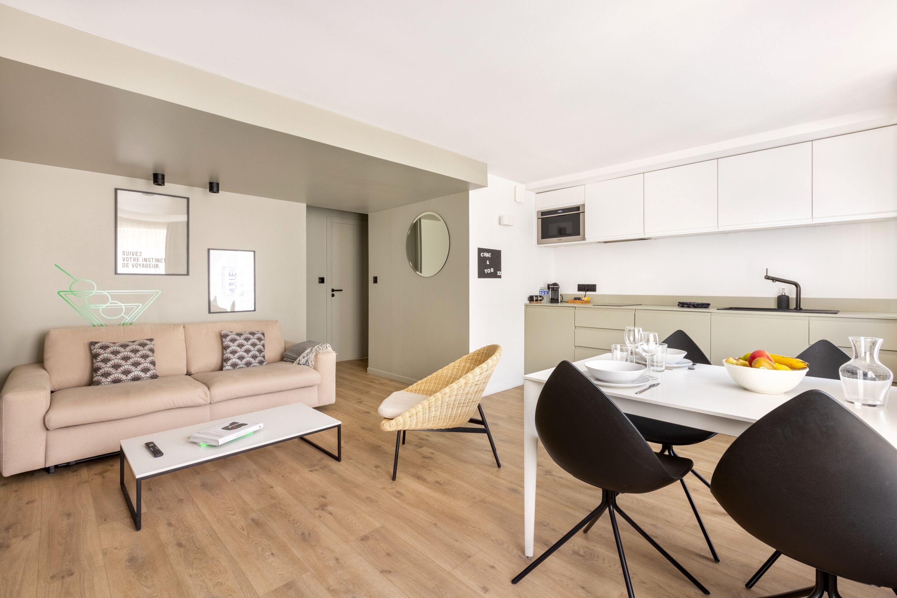 Ein modernes Wohnzimmer mit einer Couch, einem Couchtisch und einem Essbereich mit Stühlen und einem Tisch. Es gibt eine Küche mit Schränken und einer Mikrowelle.