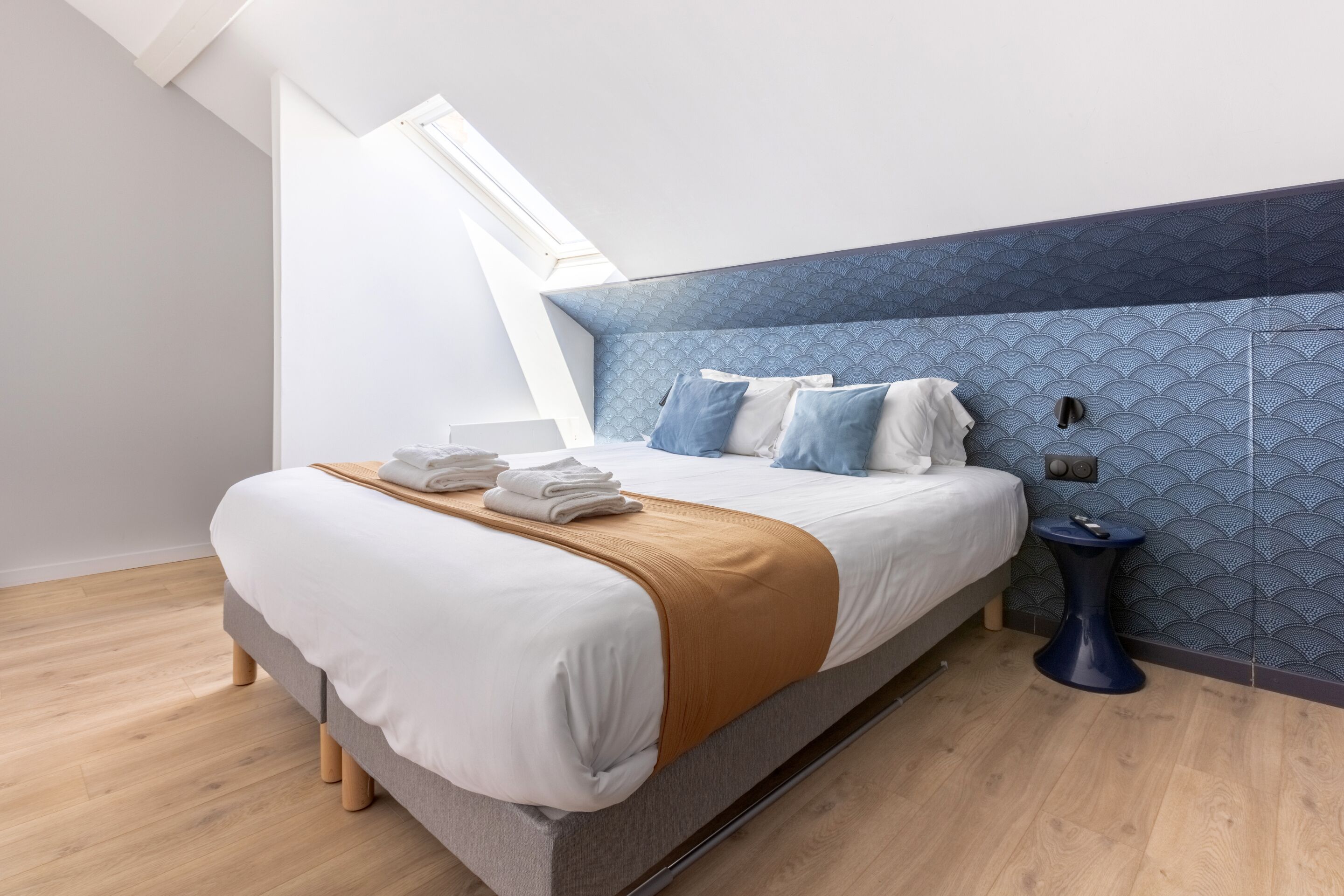 Een moderne slaapkamer met een groot bed, een blauwe accentmuur en een dakraam.