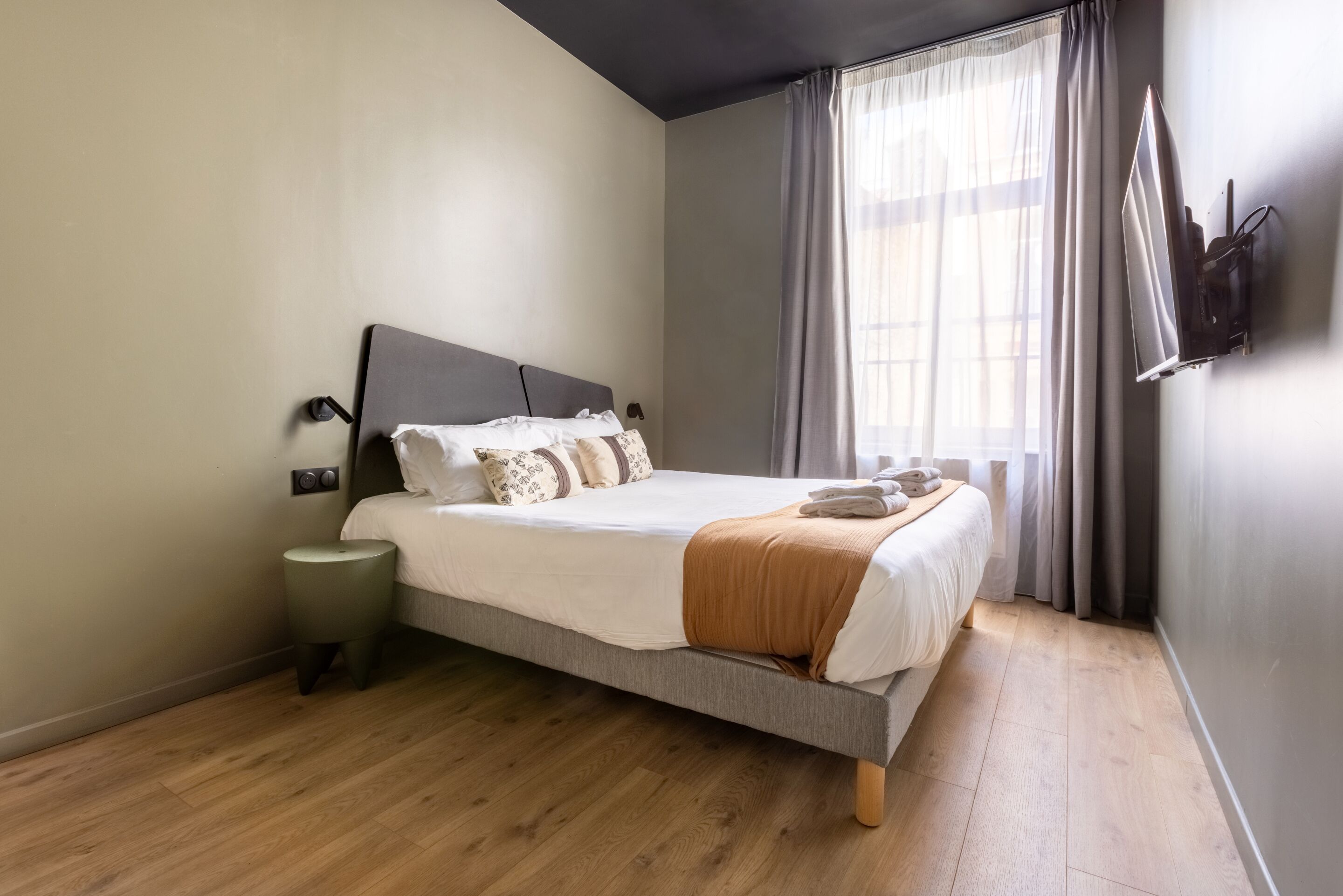 Una camera da letto moderna con un letto, un comodino e una TV a parete.