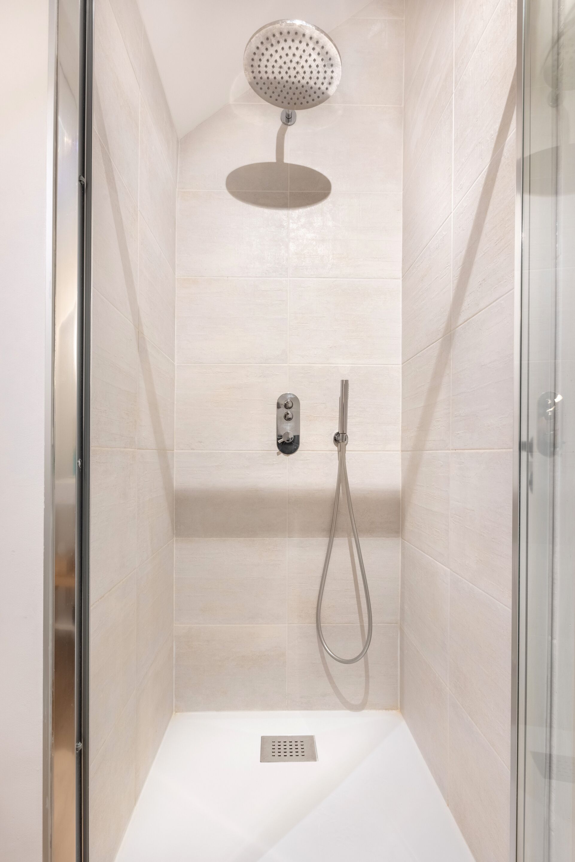 A modern shower with a handheld showerhead and a wall-mounted control panel.
