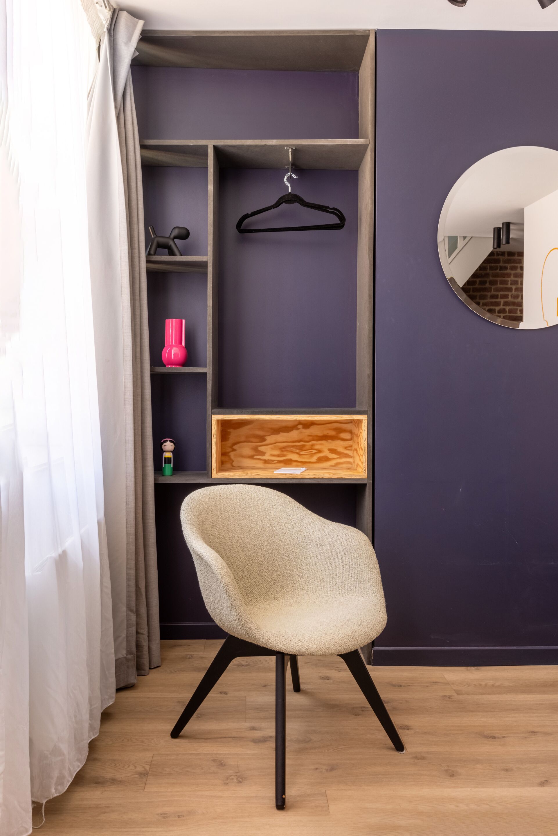 Una habitación con una silla, un estante de madera, un perchero negro colgante y un espejo en la pared.