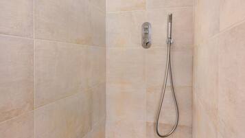 A shower with a handheld showerhead, a wall-mounted control panel, and a drain.