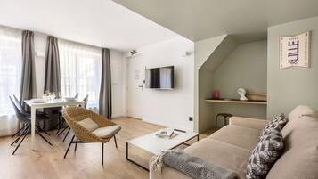 Een moderne woonkamer met een bank, een eettafel en een aan de muur bevestigde televisie.