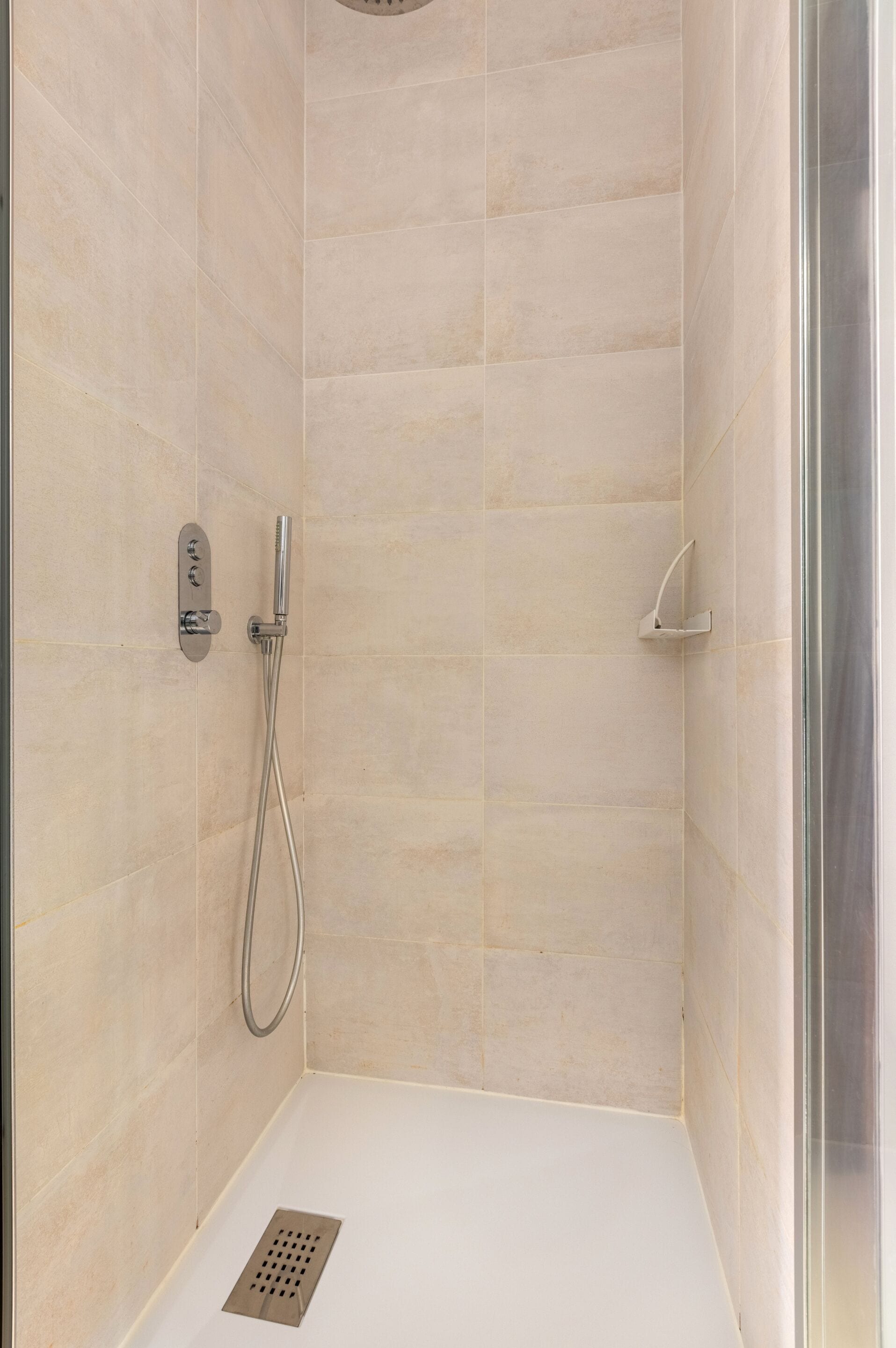 Une douche équipée d’un pommeau de douche à main et d’un robinet fixé au mur.
