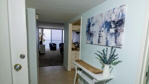 Un pasillo con una puerta blanca, un banco, una planta en maceta y un cuadro en la pared.