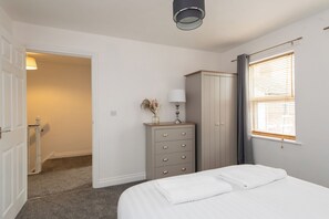 A bedroom with a bed, a dresser, a window with blinds, and a door leading to another room. - Toast Stays - The Vale House (Shildon)