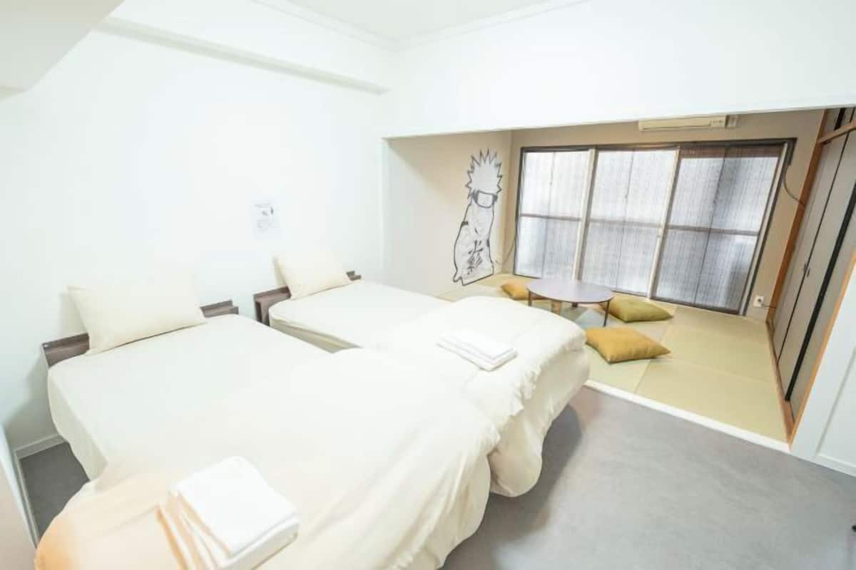 A hotel room with two beds, a small table, a window with curtains, and a wall with a drawing.