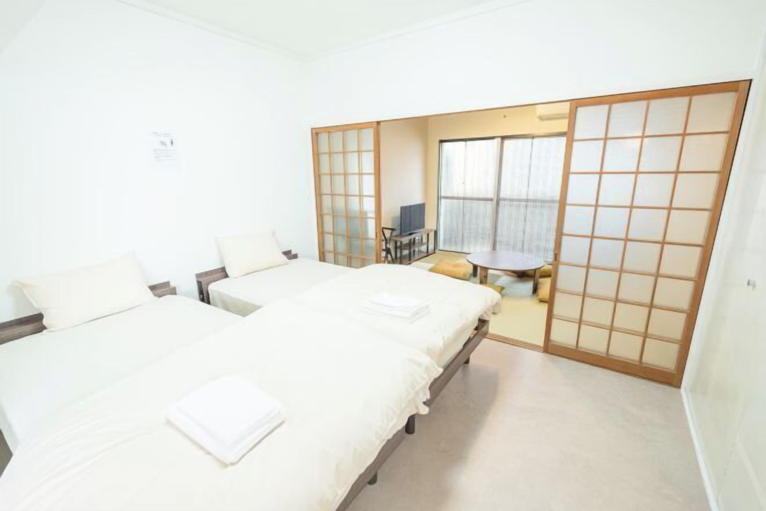 A room with two beds, a small table, and a sliding door leading to another room.