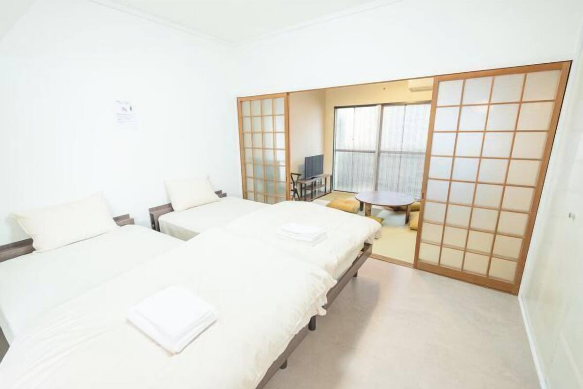 A room with two beds, a small table, and a sliding door leading to another room.