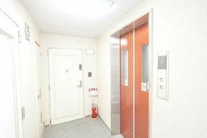 A hallway with a white door, an elevator, and a fire extinguisher. - Apartment in Nishi-ku, Osaka City (Osaka)