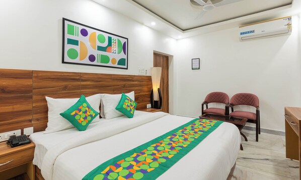 A hotel room with a wooden headboard, a bed with white bedding, two green and purple pillows, a green and orange decorative runner, a desk with a telephone, and a chair with a red cushion. - Treebo Buddha Pride (Patna)