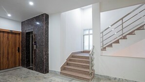 Ein modernes Interieur mit einer Marmortreppe, einer Holztür und einem digitalen Bedienfeld für den Aufzug.
