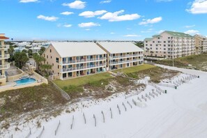 A beachfront hotel with multiple-story buildings, a swimming pool, and a beach area with sand and wooden barriers. - Crystal Villas B9 New Listing Specials! Gulf Front, Pool, Free Beach Service (Destin)