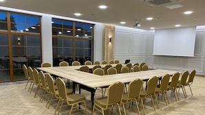 A conference room with a large rectangular table surrounded by chairs, a projector screen, and a large window with a view of the outside. - Azretreat (gmina Ostrowite)