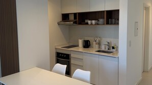 Una cuina moderna amb armaris blancs, forn integrat i zona de menjador amb taula i cadires blanques.