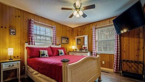 A wooden-paneled bedroom with a bed, nightstand, lamp, ceiling fan, and a TV. - Sleepy Bear Ranch-Sleeps 11 FENCED DOG AREA-Easy Roads-Firepit+Arcade (Sevierville)