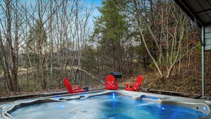 Ein Whirlpool mit drei roten Adirondack-Stühlen, umgeben von Bäumen.