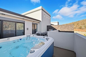 Un espace extérieur moderne doté d’un bain à remous, offrant une vue dégagée sur le paysage environnant, ainsi qu’une terrasse avec des sièges et une structure architecturale contemporaine.