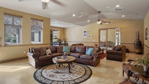 A spacious living room with a large brown leather sectional sofa, a coffee table, and a patterned rug. There are ceiling fans, recessed lighting, and large windows with blinds. - The Grand Retreat - Brand New! (Hurricane)