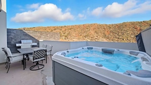 A hot tub with a table and chairs, a stone wall, and a view of a hilly landscape. - The Grand Retreat - Brand New! (Hurricane)