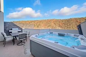 A hot tub with a table and chairs, a stone wall, and a view of a hilly landscape. - The Grand Retreat - Brand New! (Hurricane)