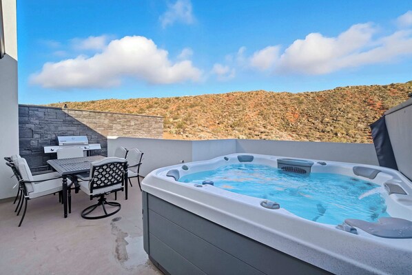 A hot tub with a table and chairs, a stone wall, and a view of a hilly landscape.