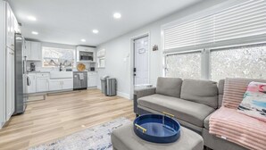 A modern apartment with a kitchen, a living area with a sofa and a coffee table, and a large window with blinds. - La Casita - Stay for 6 Guests (Tampa)