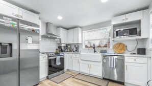 A modern kitchen with stainless steel appliances, white cabinetry, and a wooden cutting board on the countertop. - La Casita - Stay for 6 Guests (Tampa)