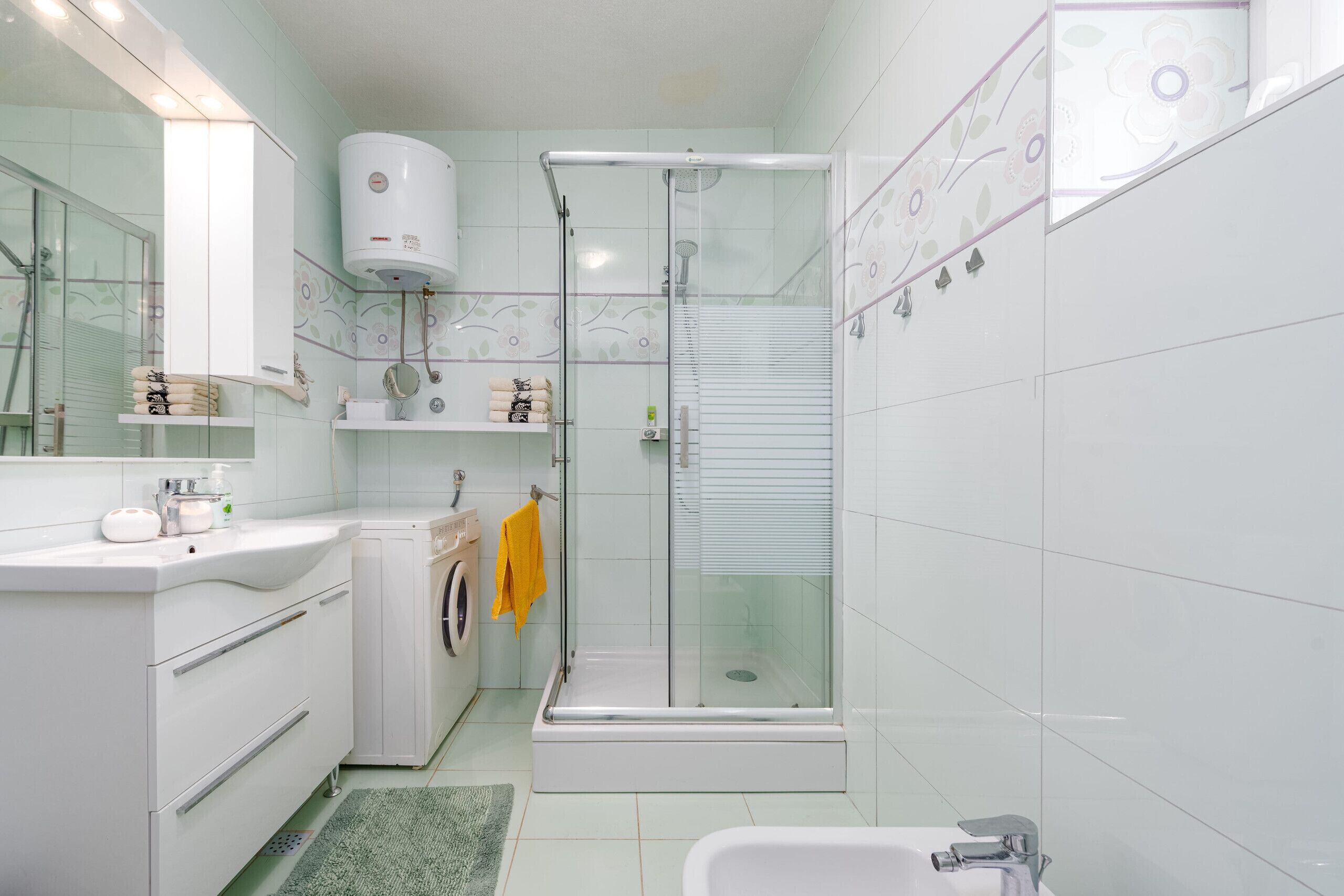 A modern bathroom with a glass-enclosed shower, a white sink, and a built-in washing machine.