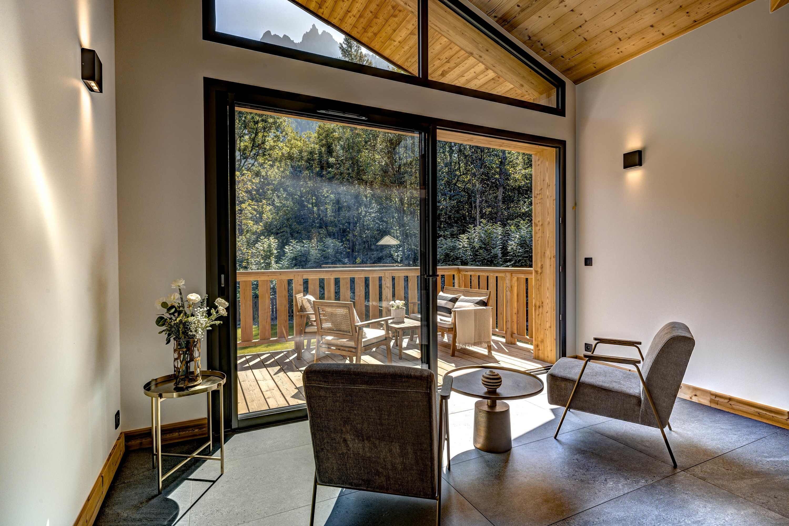 A spacious balcony with a wooden deck, furnished with chairs and a table, overlooking a mountainous landscape.