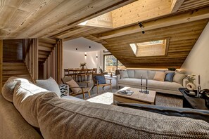 Een gezellig, houten interieur met een schuine kap, een bank, een bijzettafeltje en een eethoek.