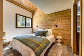 Ein Schlafzimmer mit Holzboden, einem großen Bett mit vielen Kissen, einem Nachttisch und einem Fenster mit Blick auf Bäume.