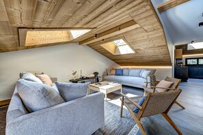 Een loft-achtige woonruimte met een hoge plafond, dakramen, een zithoek, een salontafel en een rieten fauteuil.