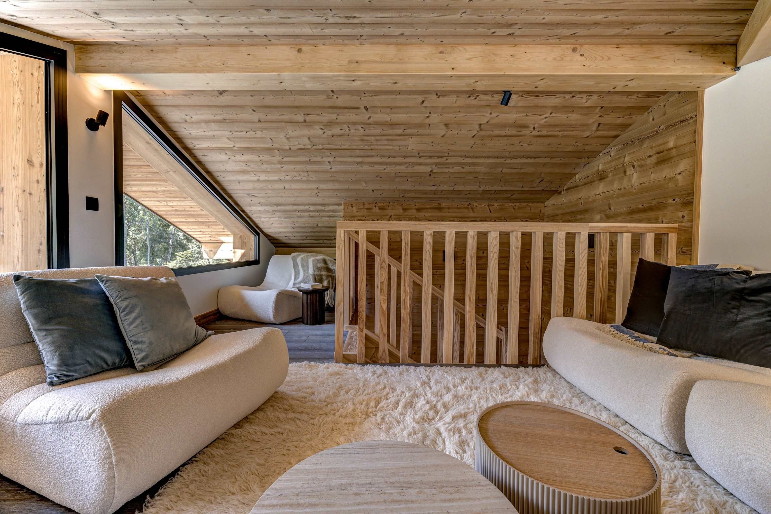 Un intérieur chaleureux avec un plafond en bois, un canapé, une table ronde et une vue par la fenêtre.