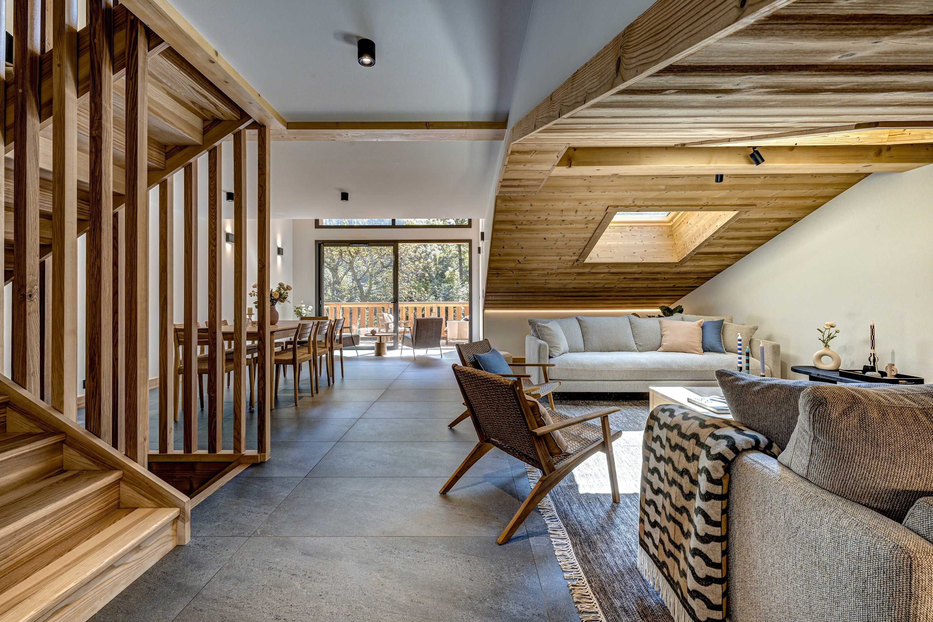 A spacious living area with a high ceiling, wooden beams, a sofa, a chair, and a dining table.