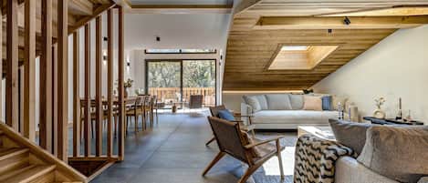 A spacious living area with a high ceiling, wooden beams, a sofa, a chair, and a dining table.