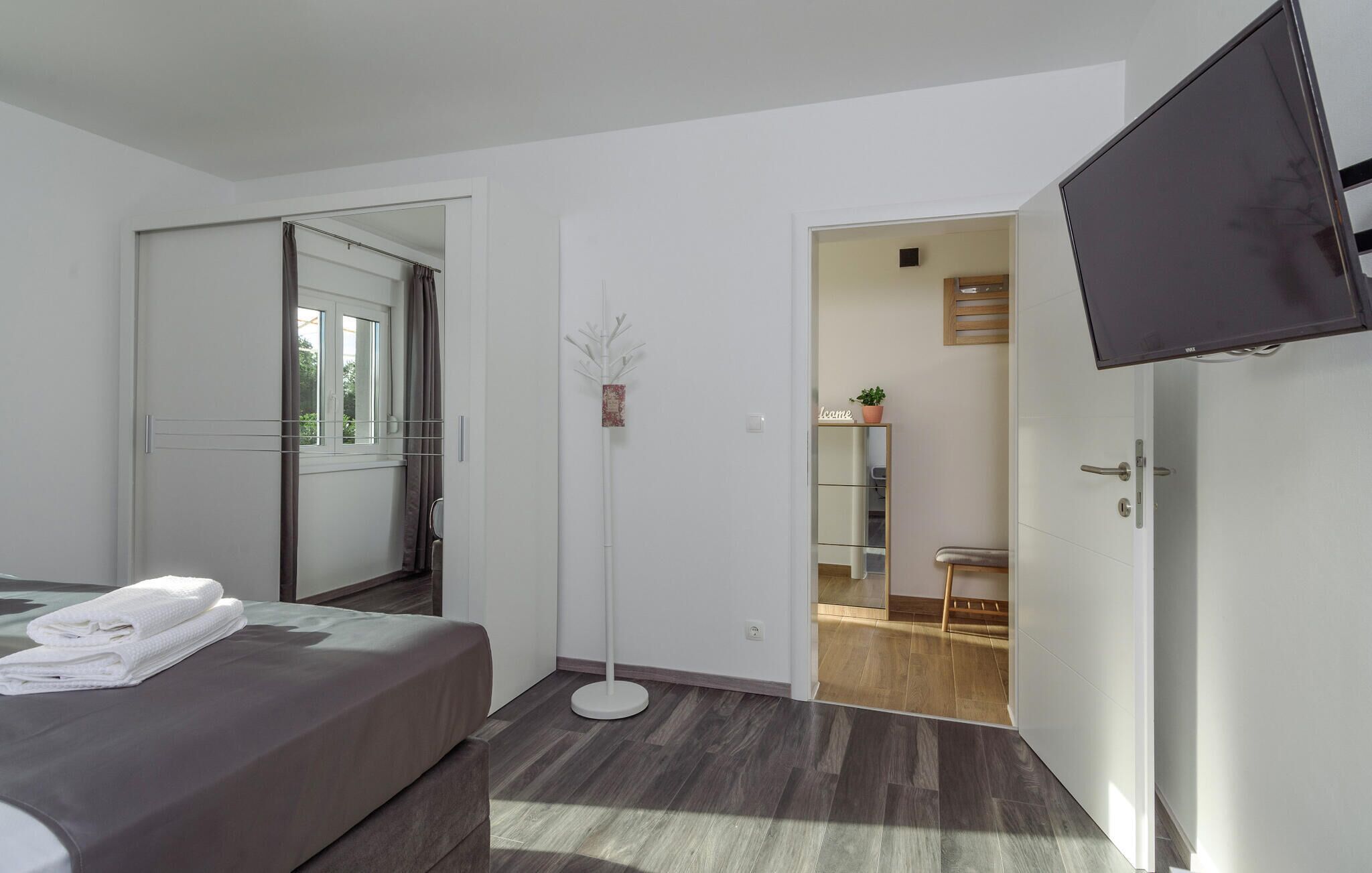 A modern bedroom with a bed, a bedside table, a floor lamp, and a TV mounted on the wall.