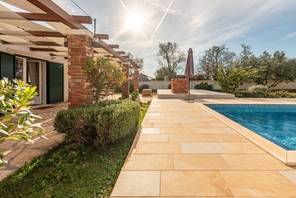Zona de piscina con pérgola, pilares de ladrillo y patio empedrado.