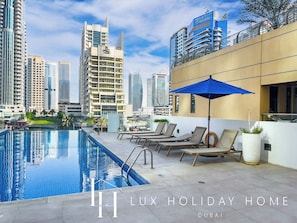 A rooftop pool with lounge chairs and a blue umbrella, surrounded by high-rise buildings.