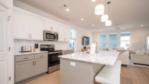 Een moderne keuken met witte kastjes, roestvrijstalen apparatuur en een marmeren eiland met zitplaatsen.