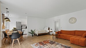 Un espace de vie moderne comprenant une table à manger en bois, des chaises noires, un canapé et un grand tapis.