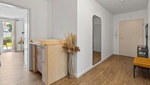 Une pièce moderne avec un plancher en bois, un bureau en bois doté de tiroirs, un miroir, un banc et une porte.