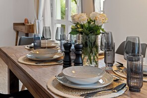 A dining table set with plates, bowls, cutlery, glasses, and a vase with flowers. - Glücksfewo71, for families, center, private underground parking space, 2 terraces, Allgäu (Kempten (Allgäu))