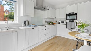 A modern kitchen with white cabinetry, a built-in stove, and a window overlooking a garden. - Morford House in Exeter (Exeter)