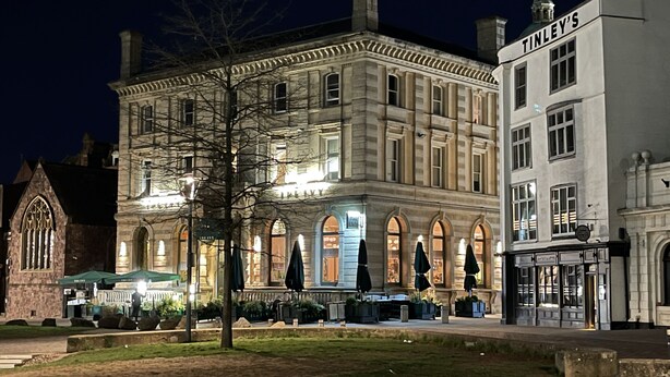 A historic building with arched windows and a corner entrance, featuring outdoor seating and a well-lit facade. - Morford House in Exeter (Exeter)
