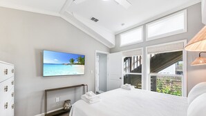 Een slaapkamer met een groot bed, een aan de muur bevestigde televisie en uitzicht op de omgeving door de ramen.