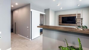 Un interior moderno con estante de madera, televisor montado y luces empotradas en el techo.